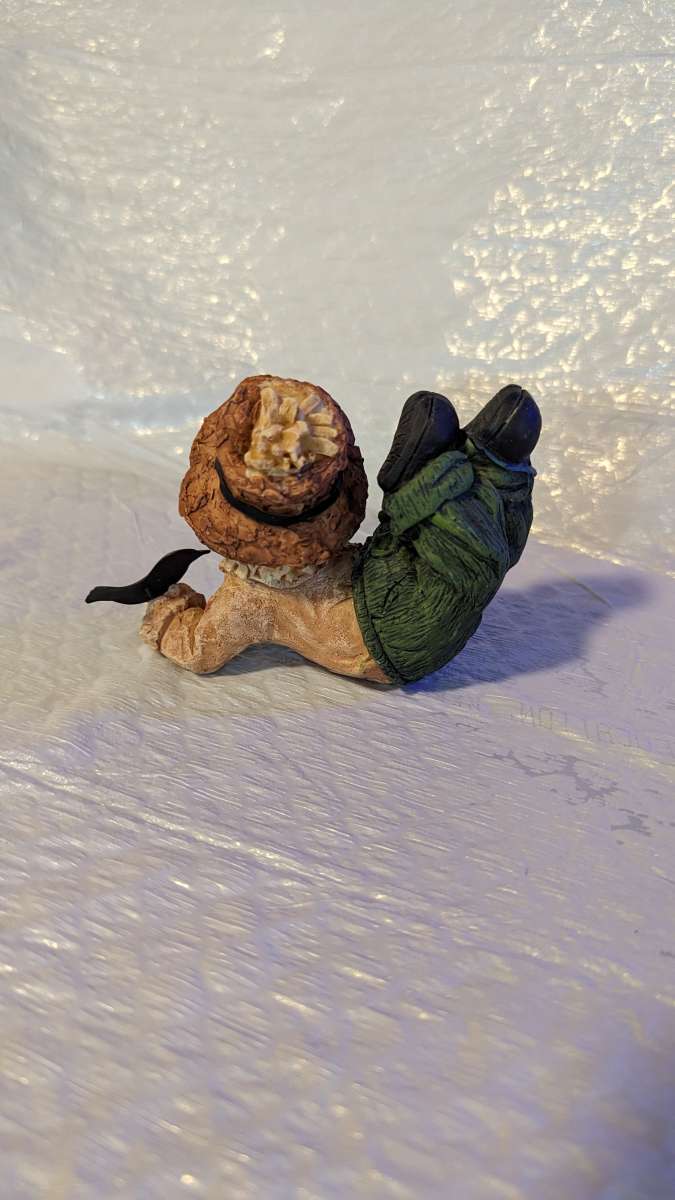 Resin Scarecrow Laying Down With Legs Bent Holding A Crow