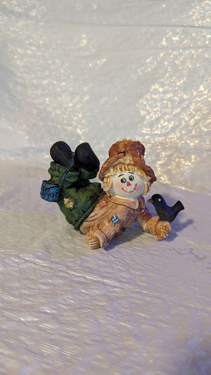 Resin Scarecrow Laying Down With Legs Bent Holding A Crow
